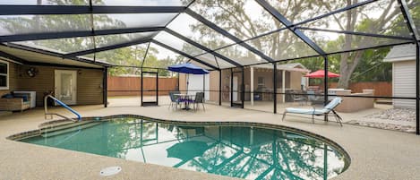 Una piscina techada con un área de patio, que incluye una mesa y sillas, y vista al jardín trasero.