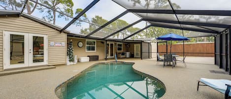 A covered outdoor swimming pool with a patio area, a wooden fence, and a blue umbrella.