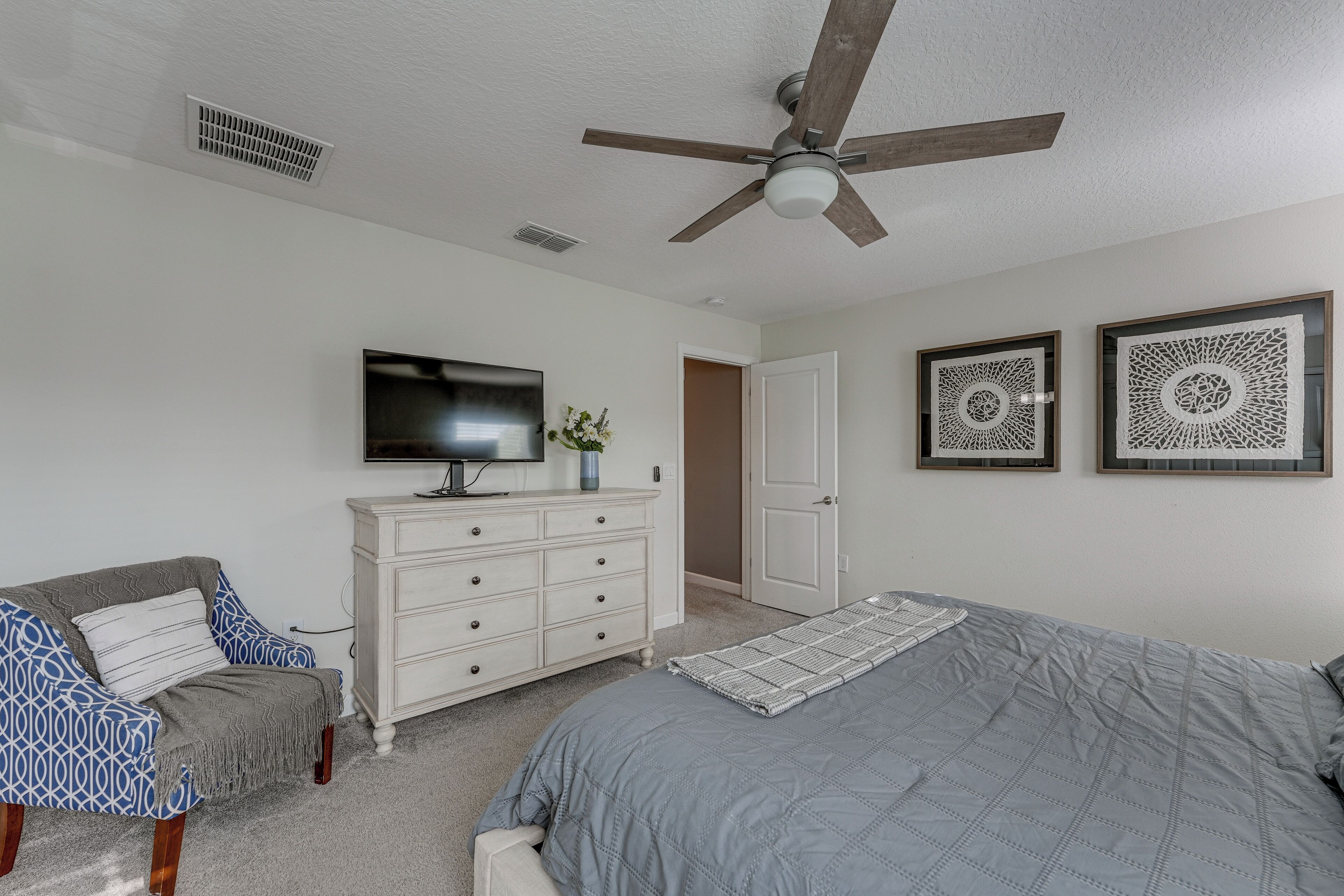 A bedroom with a bed, a dresser, a television, and two decorative wall pieces.