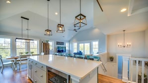 A spacious kitchen with a large island, pendant lighting, and a view of the outdoors. - Luxe Family Home w/ Seasonal Pool in Duck! (Kitty Hawk)