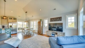 A spacious living area with a large TV, a dining area, and a kitchen with a refrigerator. - Luxe Family Home w/ Seasonal Pool in Duck! (Kitty Hawk)
