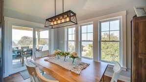 A dining area with a wooden table, chairs, a woven placemat, and a pendant light. - Luxe Family Home w/ Seasonal Pool in Duck! (Kitty Hawk)