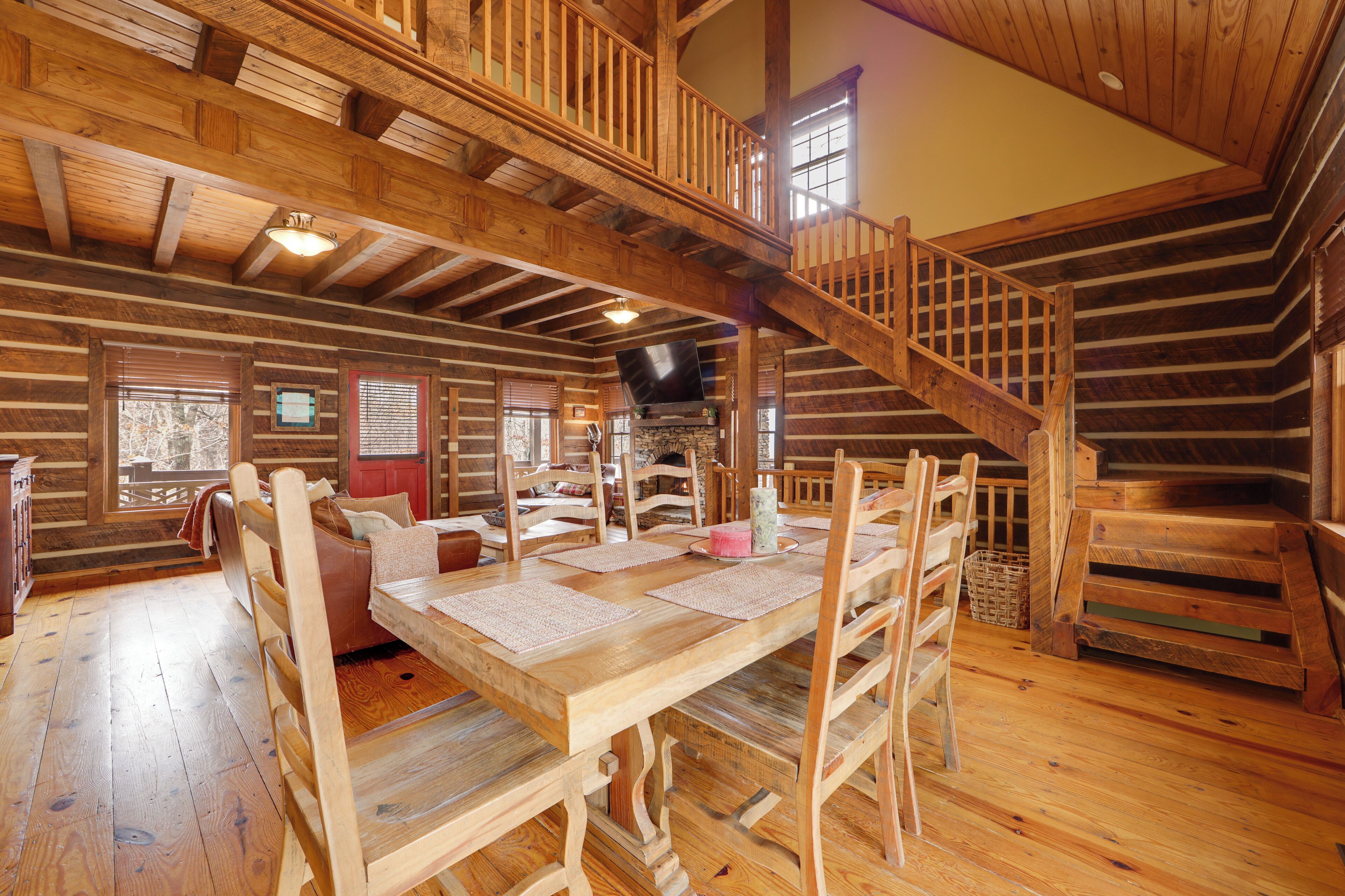 Interior de una cabaña de troncos con una mesa de comedor de madera, sillas, un sofá y una escalera.