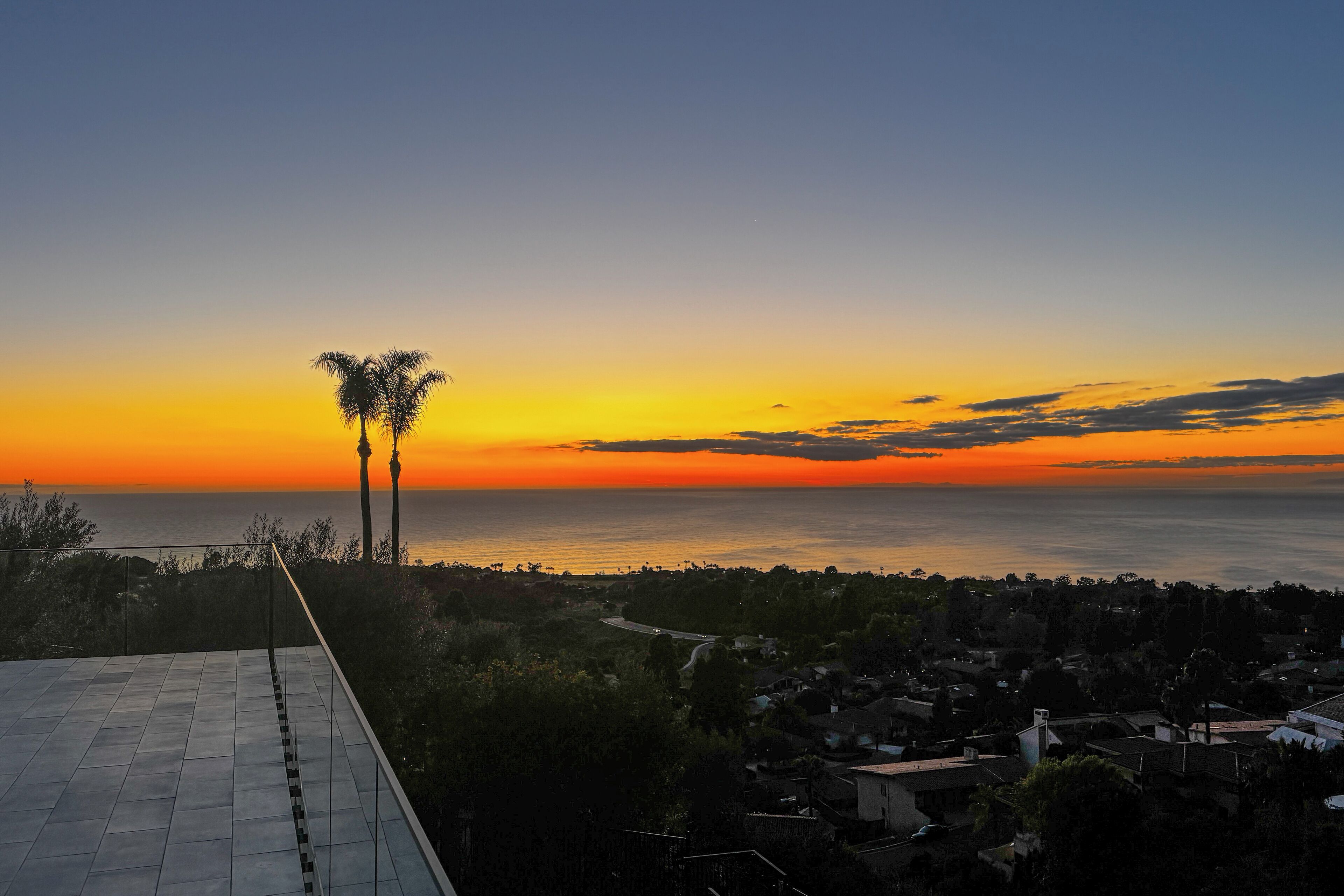 A sunset view from a rooftop terrace overlooking a coastal town.