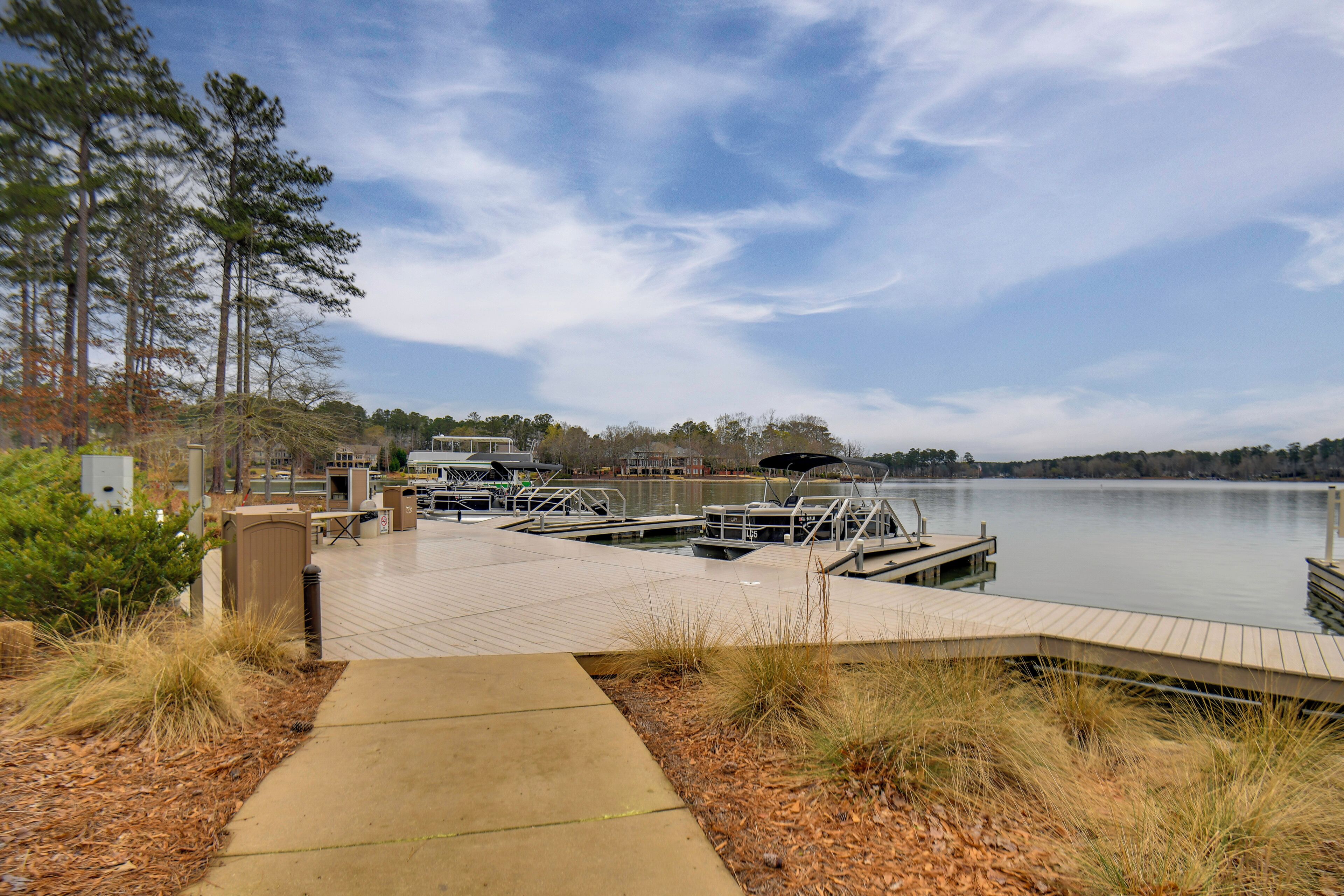 A dock with boats, a concrete pathway, and a lake with trees in the background.