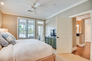 A bedroom with a bed, a ceiling fan, a TV, and a view of the outside through the window.
