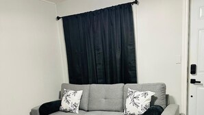 A modern living room with a grey sectional sofa, black and white patterned cushions, a round wooden coffee table, and a ceiling fan.