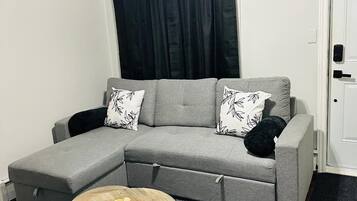 Uma sala de estar moderna com um sofá seccional cinza, almofadas estampadas em preto e branco, uma mesa de centro redonda de madeira e um ventilador de teto.