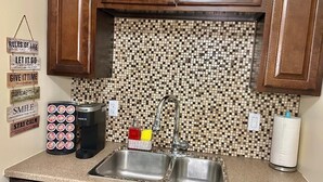 A kitchen with a tiled backsplash, a coffee maker, a paper towel holder, and a set of mugs.