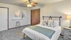 Ein Schlafzimmer mit Bett, Deckenventilator, Nachttisch, Schreibtisch und einer Tür.