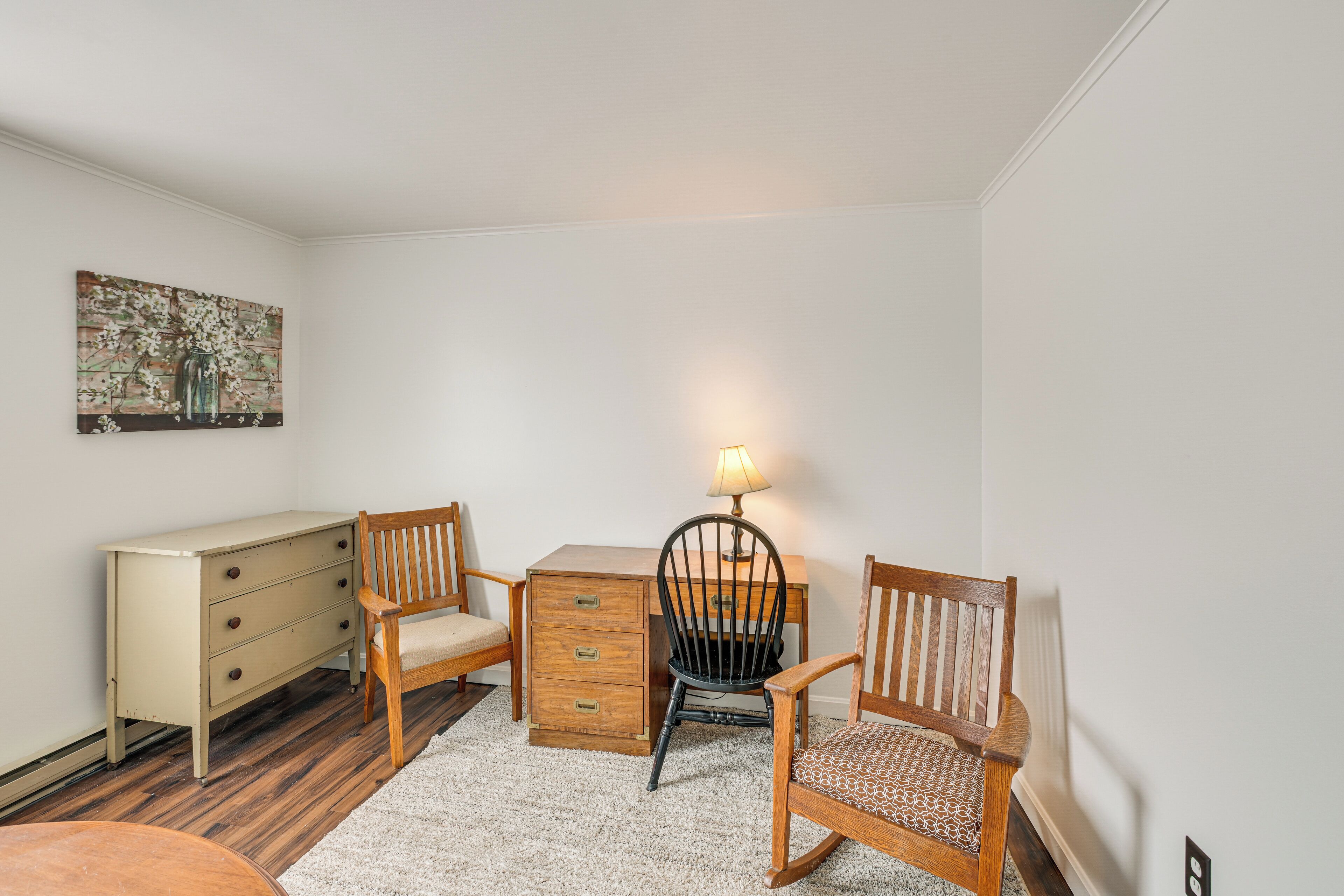 A room with a desk, two chairs, a dresser, and a lamp.