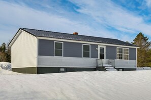A single-story house with a dark roof and light siding, surrounded by snow. - Walk to Restaurants & Markets: Machias Home! (Machias)
