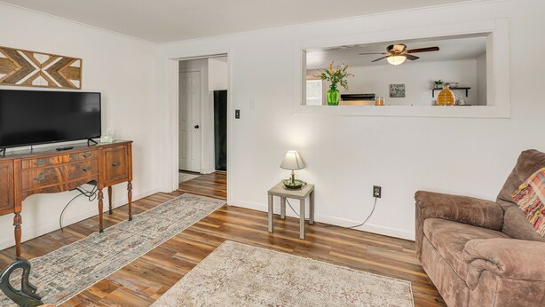 A living room with a wooden floor, a brown sofa, a TV on a wooden cabinet, a small table with a lamp, and a mirror on the wall. - Walk to Restaurants & Markets: Machias Home! (Machias)