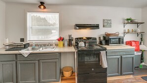 A kitchen with a stove, microwave, sink, and wooden flooring. - Walk to Restaurants & Markets: Machias Home! (Machias)