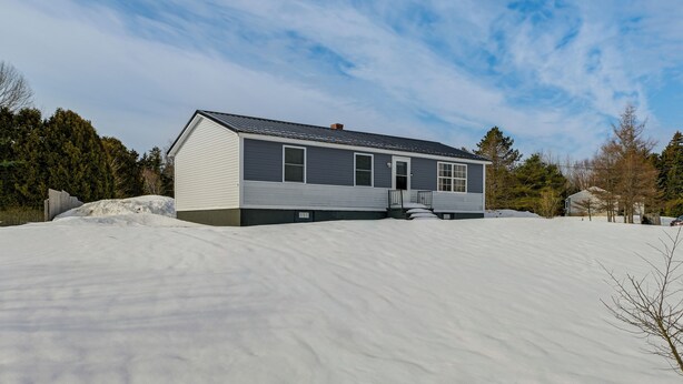 A single-story house with a gray exterior and a dark roof, surrounded by a snowy landscape and trees. - Walk to Restaurants & Markets: Machias Home! (Machias)