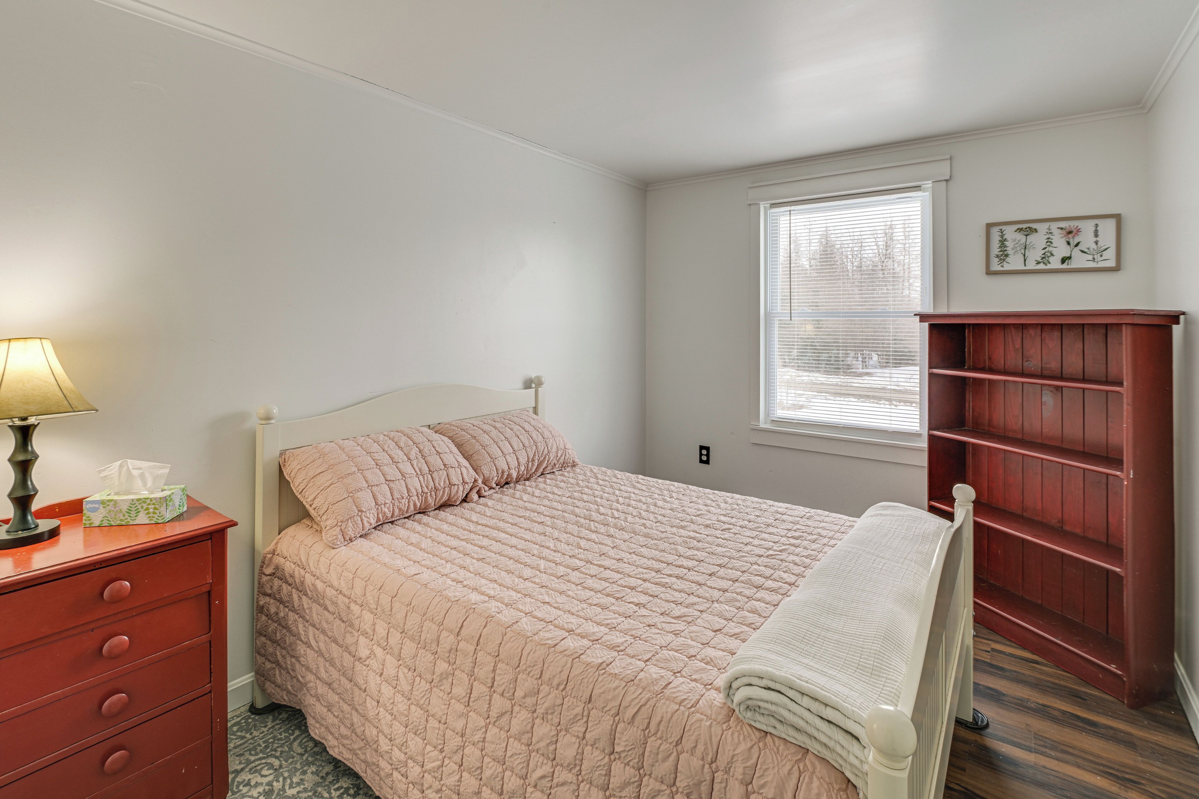 A bedroom with a bed, a dresser, a nightstand, a window with blinds, and a bookshelf.