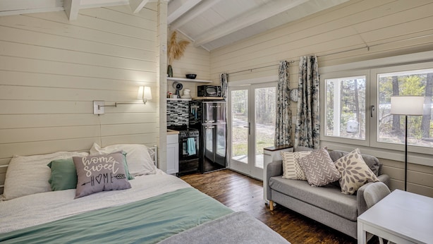 A cozy room with a bed, a sofa, a kitchenette, and a large window. - Tiny Home on Working Farm Near Amelia Island! (Yulee)