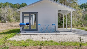 A small, single-story building with a covered patio area, a sliding glass door, and two blue folding chairs. - Tiny Home on Working Farm Near Amelia Island! (Yulee)