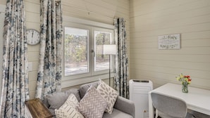 A room with a sofa, a table, a chair, a clock, a radiator, and a window with curtains. - Tiny Home on Working Farm Near Amelia Island! (Yulee)