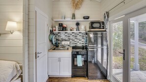 A compact kitchen with white cabinetry, a stainless steel refrigerator, a microwave, and a sink. - Tiny Home on Working Farm Near Amelia Island! (Yulee)