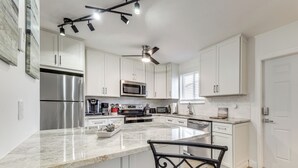 A modern kitchen with white cabinets, stainless steel appliances, a marble countertop, and a ceiling fan. - Pool Access, 1 Mi to Pier! Pompano Beach Condo (Pompano Beach)