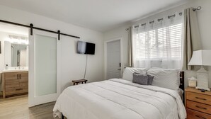 A bedroom with a bed, a TV mounted on the wall, a bedside table with a lamp, and a wooden dresser. - Pool Access, 1 Mi to Pier! Pompano Beach Condo (Pompano Beach)