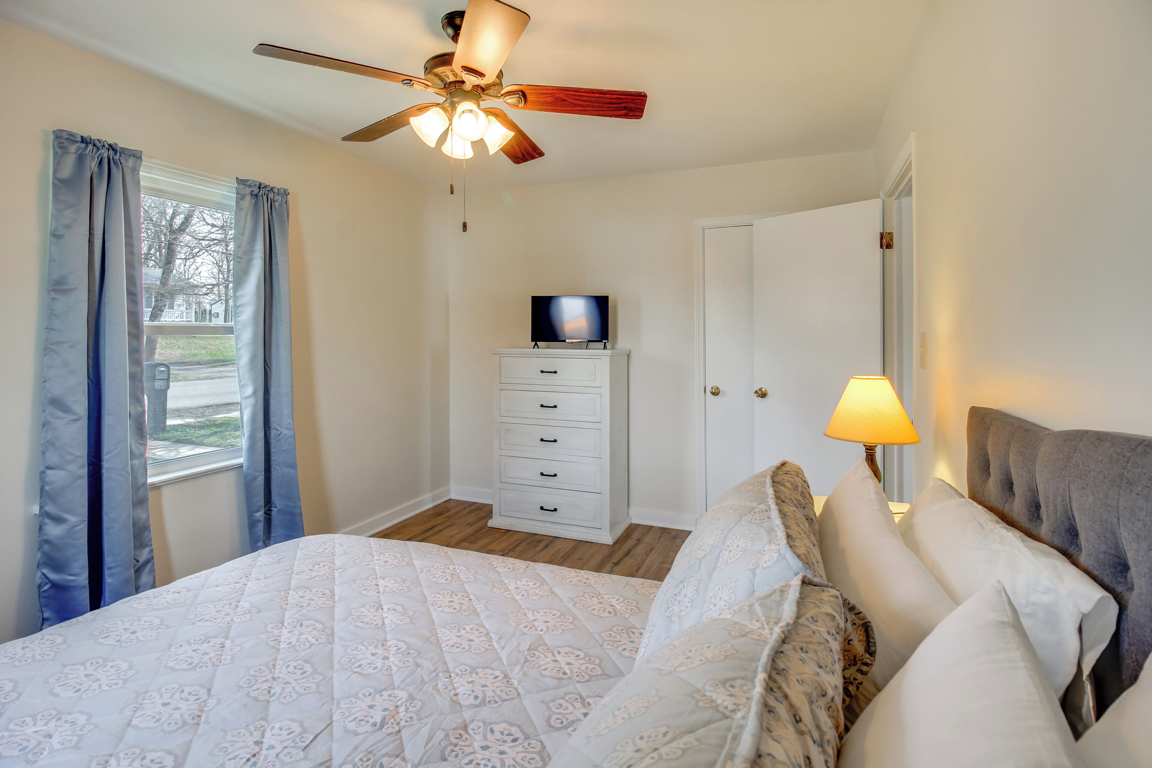 A bedroom with a bed, a ceiling fan, a dresser, a television, and a lamp.