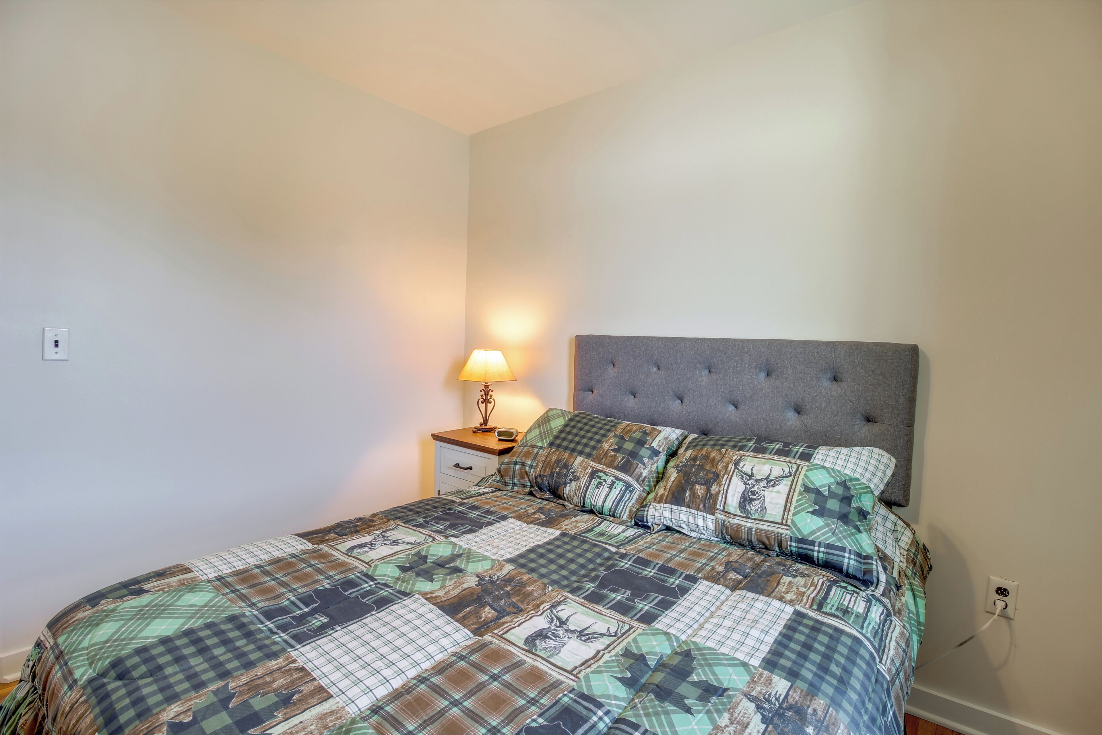 Un dormitorio con cama, una mesita de noche con lámpara y un enchufe de pared.
