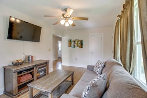 A living room with a flat-screen TV, wooden entertainment unit, sofa, and a ceiling fan. - Lakes, Whiskey & More! Charming Home in Tullahoma (Tullahoma)