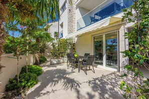 An outdoor patio with a table and chairs, surrounded by greenery and a stone wall. - Modern ground-floor apartment with a pool and private parking (Crikvenica)