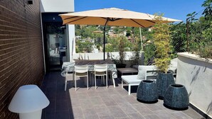 Un patio con una mesa, sillas, una sombrilla grande y plantas en macetas.