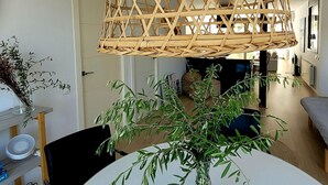 Un comedor con una mesa redonda, sillas, un florero transparente con follaje verde y una lámpara colgante de fibras naturales.