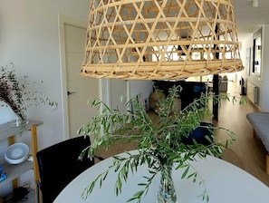 A dining area with a round table, chairs, a clear vase with green foliage, and a woven hanging light fixture. - Stylish Modern Villa on the Outskirts of Sitges (L'Hospitalet de Llobregat)