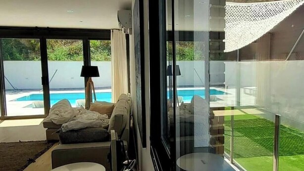 Una sala moderna con un ventanal grande, piscina visible al exterior y un rincón de descanso acogedor.