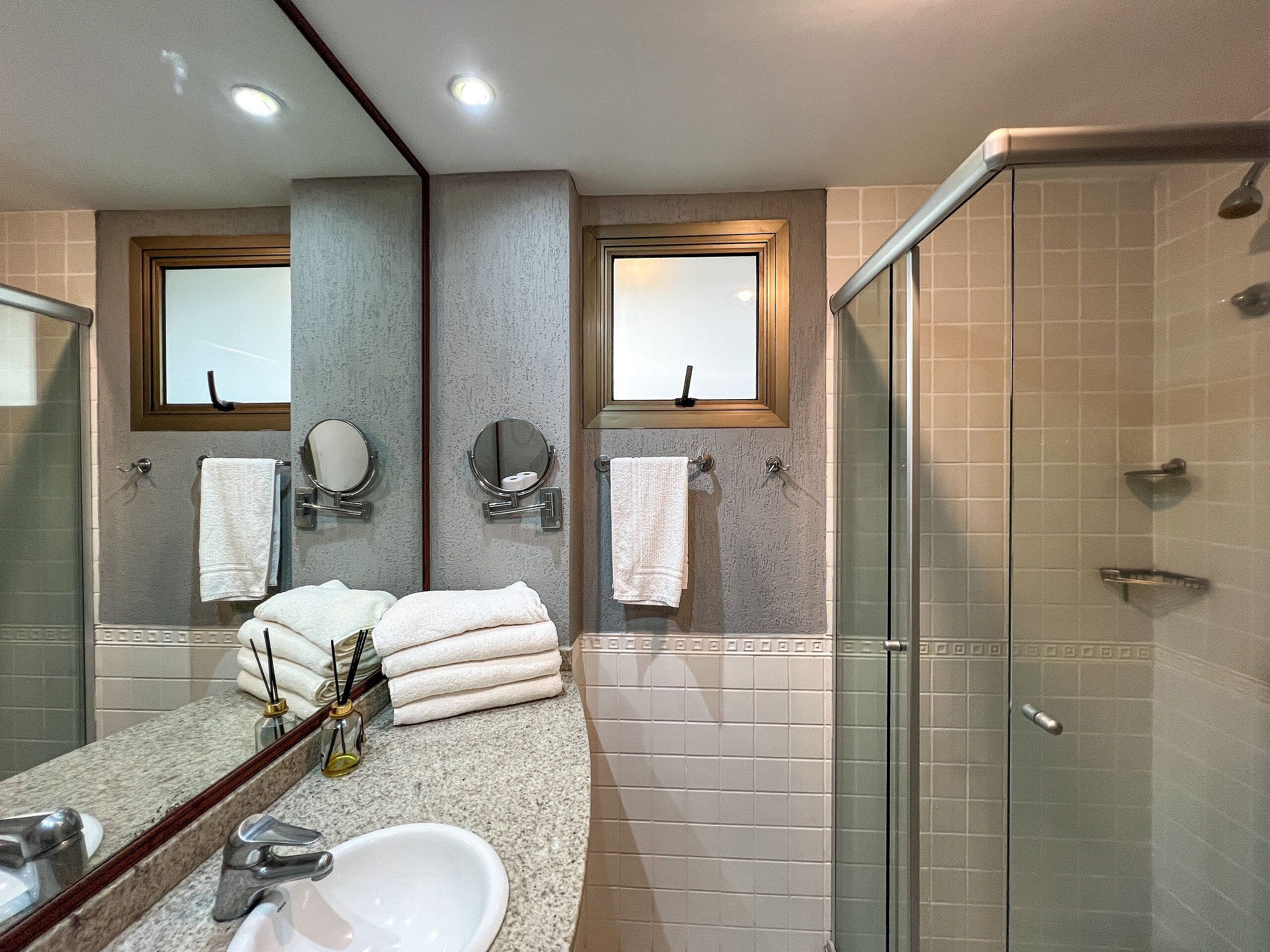 A bathroom with a sink, mirror, two towel racks, and a glass shower enclosure.