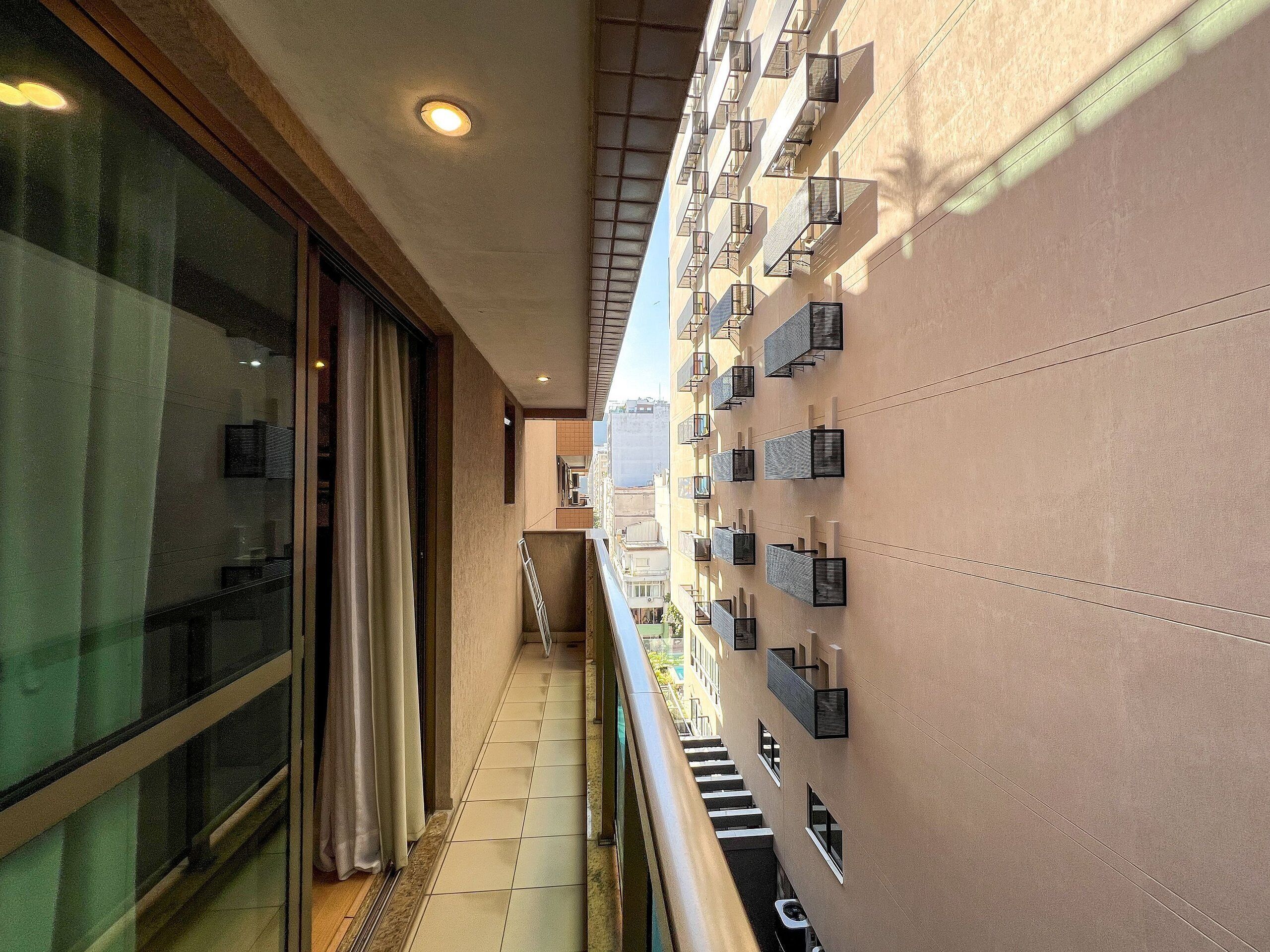 Een gang met betegelde vloer, een glazen deur en een balkon met airconditioners.