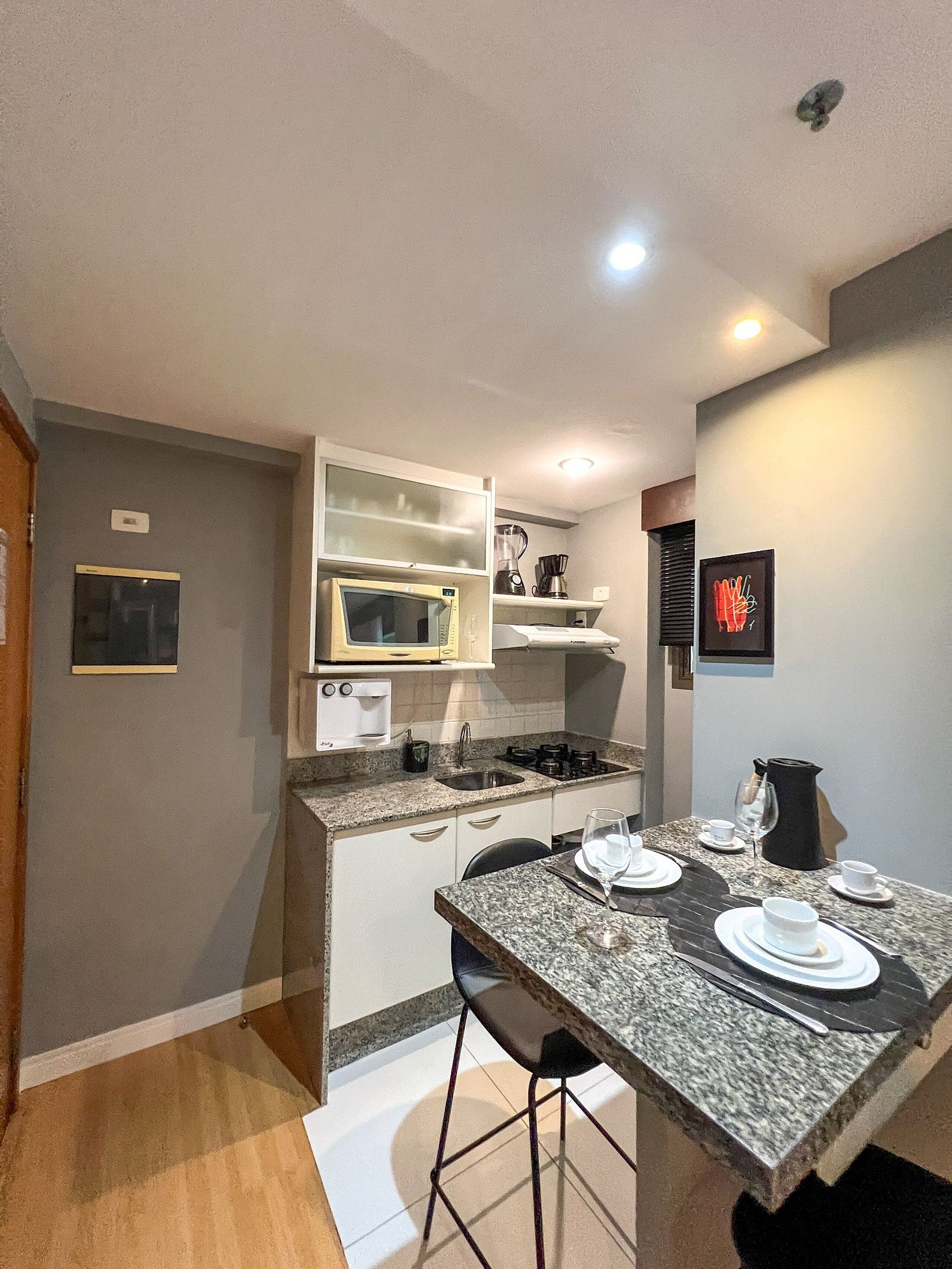 A compact kitchen with a microwave, toaster, and coffee maker, a dining area with a table set for two, and a small bar area.
