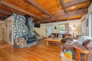 A cozy living room with a stone fireplace, wooden beams, a sofa, and a coffee table. - Mustang Sally- Free Lake Access! (Arnold)