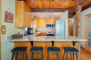 A kitchen with wooden cabinets, a central island with bar stools, a microwave, and a refrigerator. - Mustang Sally- Free Lake Access! (Arnold)
