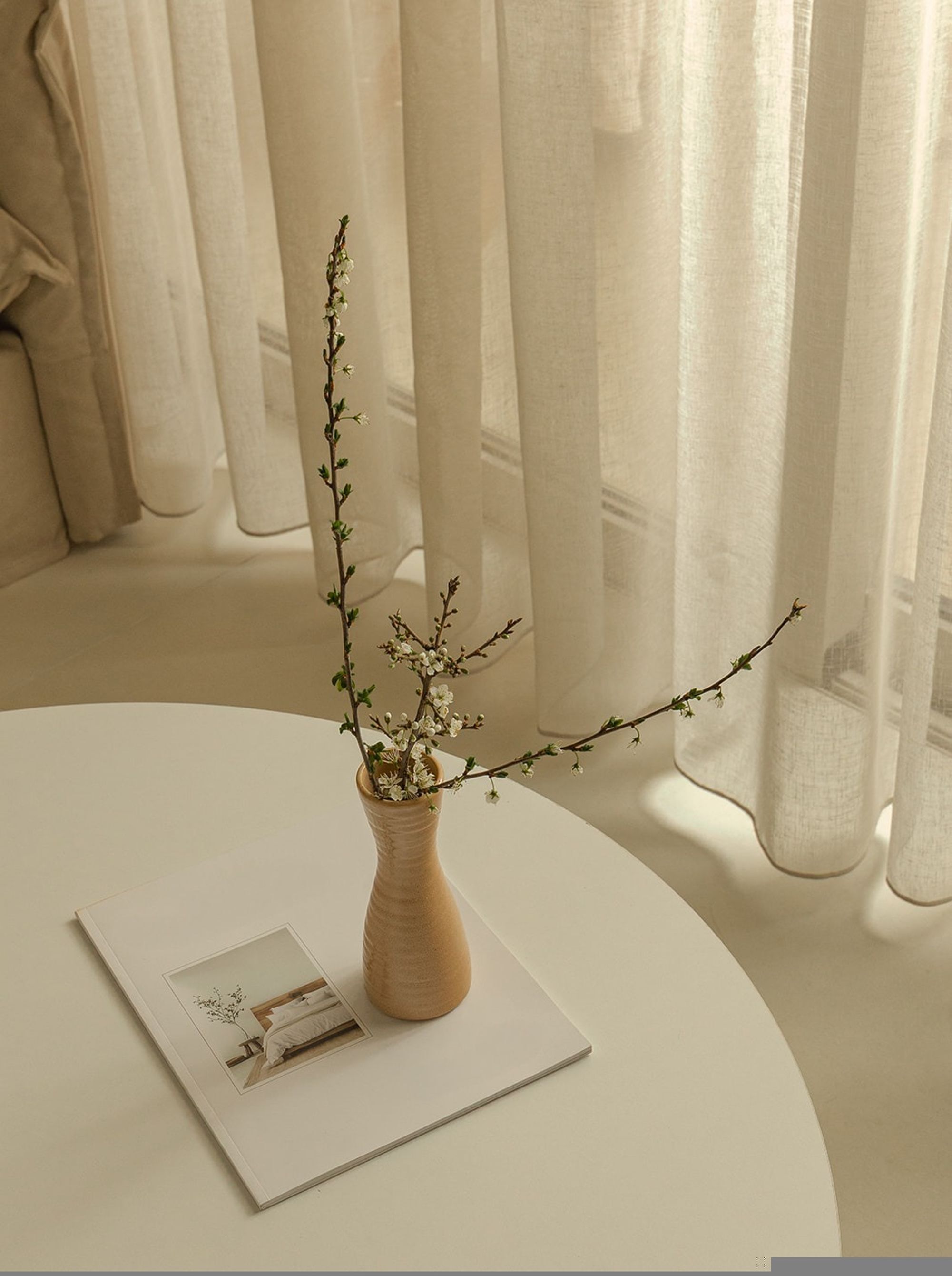A round white table with a vase of flowers and a magazine.