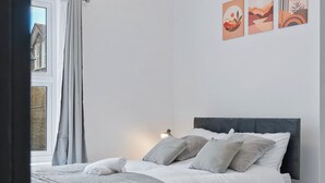Un dormitorio moderno con cama, cortinas y una obra de arte en la pared.