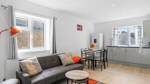 Una sala de estar moderna con un sofá gris, una mesa redonda de centro y un comedor con mesa y sillas.