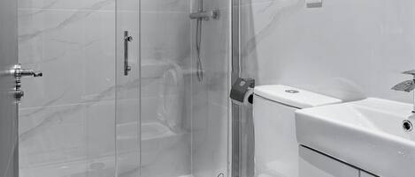 A modern bathroom with a glass-enclosed shower, a toilet, and a sink.