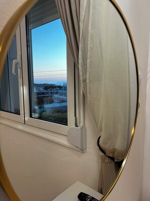 A room with a window, a round mirror, and a remote control on a table. - VDG Sunset Heaven 54sm |Gym •Netflix & Disney+ •Fully Equipped Kitchen| Rethymno (Rethymno)