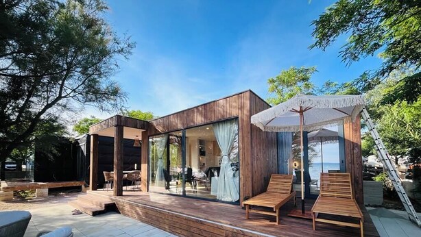 A modern outdoor patio with wooden flooring, seating areas, and a glass-enclosed space.