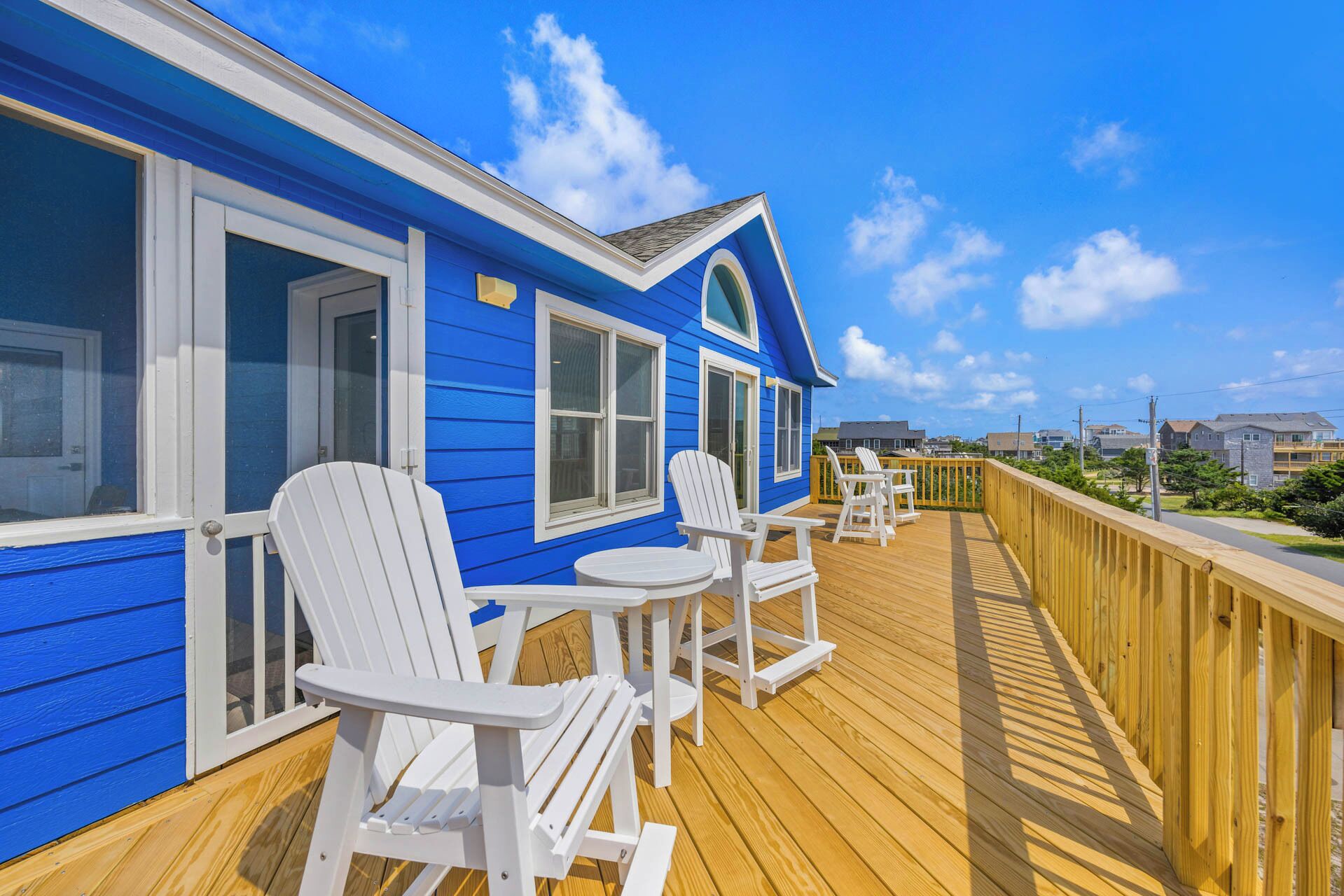 Un bâtiment bleu doté d’une terrasse en bois, de chaises blanches et offrant une vue sur les environs.