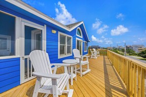 A blue building with a wooden deck, white chairs, and a view of the surrounding area. - Brand New Semi-Oceanfront Waves Home with Private Pool, Hot Tub and Game Room (Waves)
