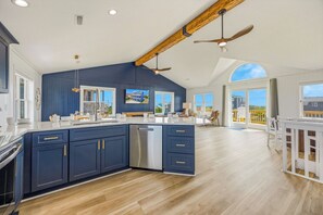 A spacious kitchen with a large island, wooden ceiling beams, and a view to the outside. - Brand New Semi-Oceanfront Waves Home with Private Pool, Hot Tub and Game Room (Waves)