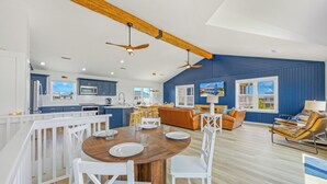A spacious kitchen with a central island, wooden ceiling beams, and a dining area with a round table and white chairs. - Brand New Semi-Oceanfront Waves Home with Private Pool, Hot Tub and Game Room (Waves)