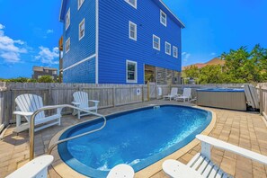 A swimming pool with a wooden deck, white lounge chairs, and a hot tub. - Brand New Semi-Oceanfront Waves Home with Private Pool, Hot Tub and Game Room (Waves)